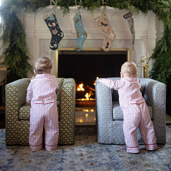 Two children in matching pajamas standing in front of a fireplace with Christmas stockings.