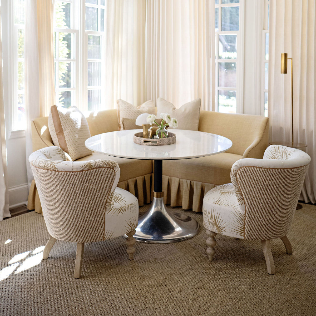 Living room with round table and chairs under large windows with white curtains